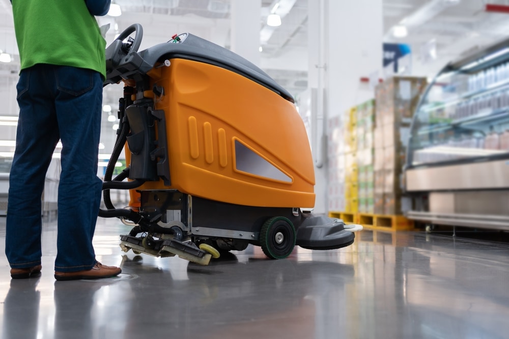 Autolaveuse industrielle : nettoyage de sol en magasin Agent nettoyant le sol d'un supermarché avec une autolaveuse industrielle orange.